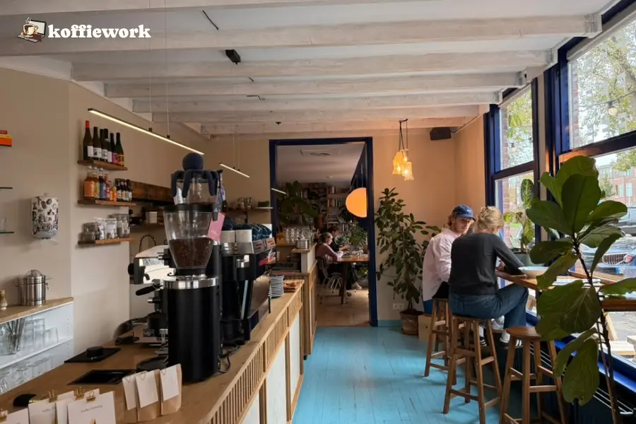 Inside Thrive in The Hague: espresso bar on the left, blue floor, big windows, and people sitting at the window counter.