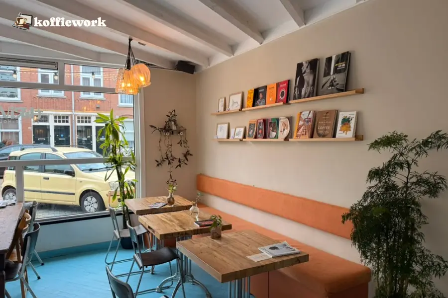 Seating area at Thrive in The Hague with wooden tables, an orange bench, magazine shelves, and a street view through the front window.