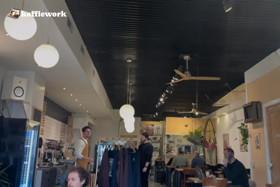 Inside Papan in The Hague: long cafe with round pendant lights, a clothing rack, and people sitting and working at tables.